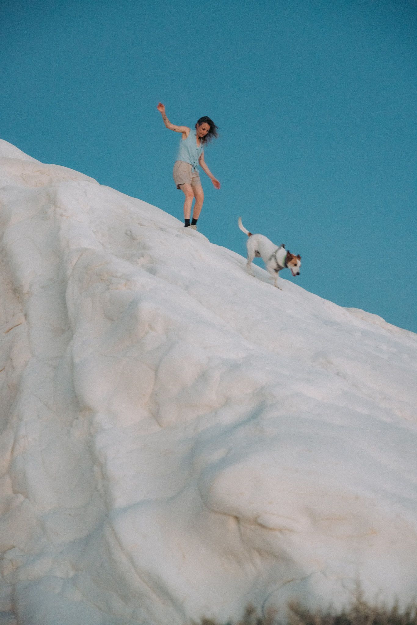 A sequence of images showing a person climbing and sliding down a steep white snowy slope against a bright blue sky.