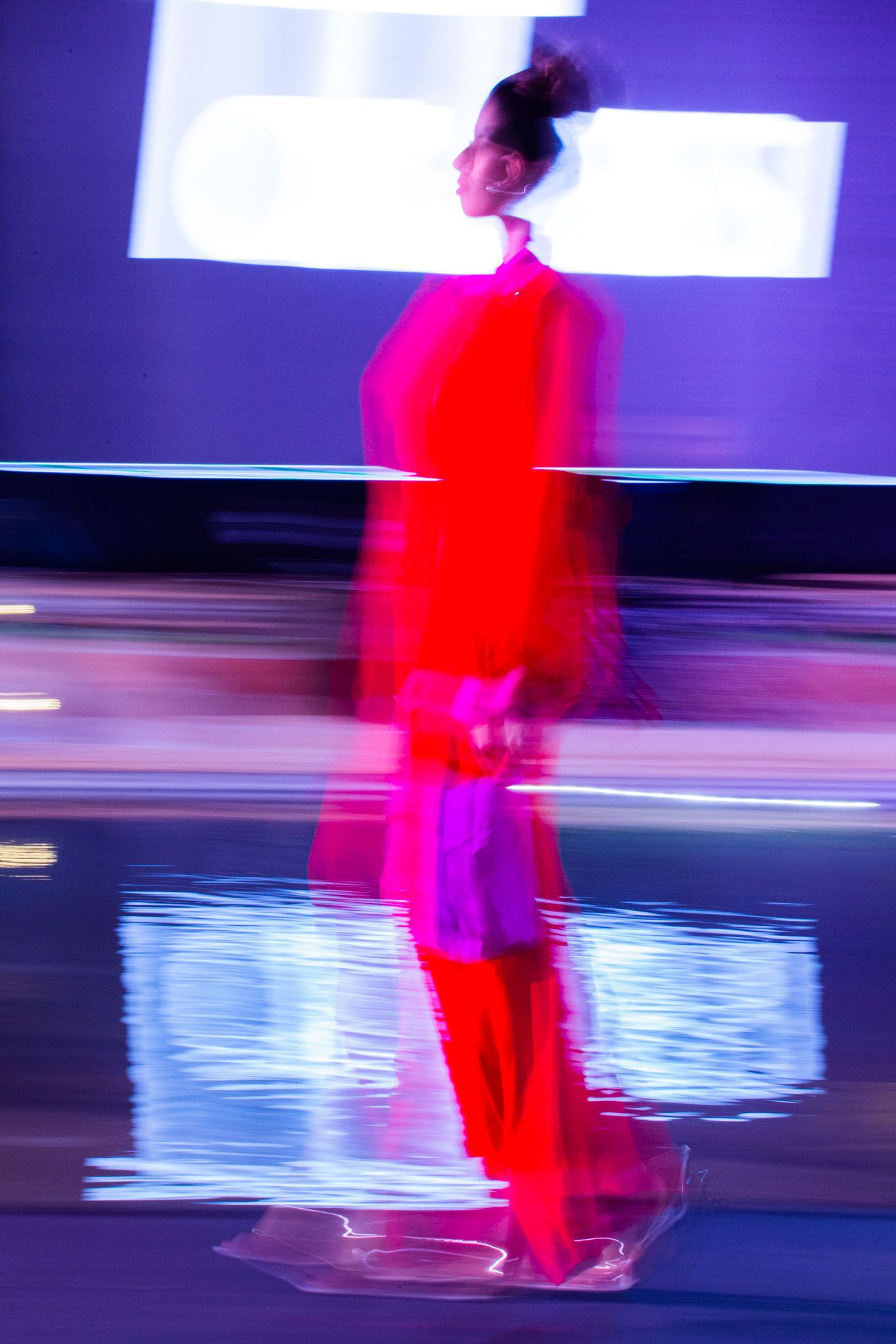 Motion-blurred figure in bright red clothing moves across a reflective blue surface against a purple background.