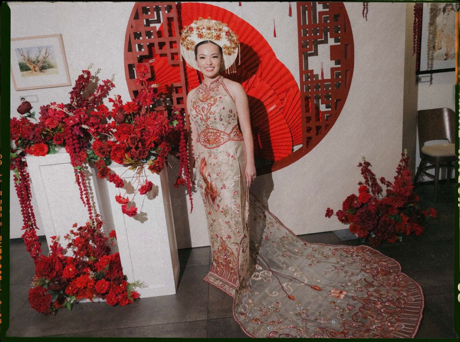 Traditional Asian bridal attire with lace train and red parasol against white wall with cherry blossom decorations.