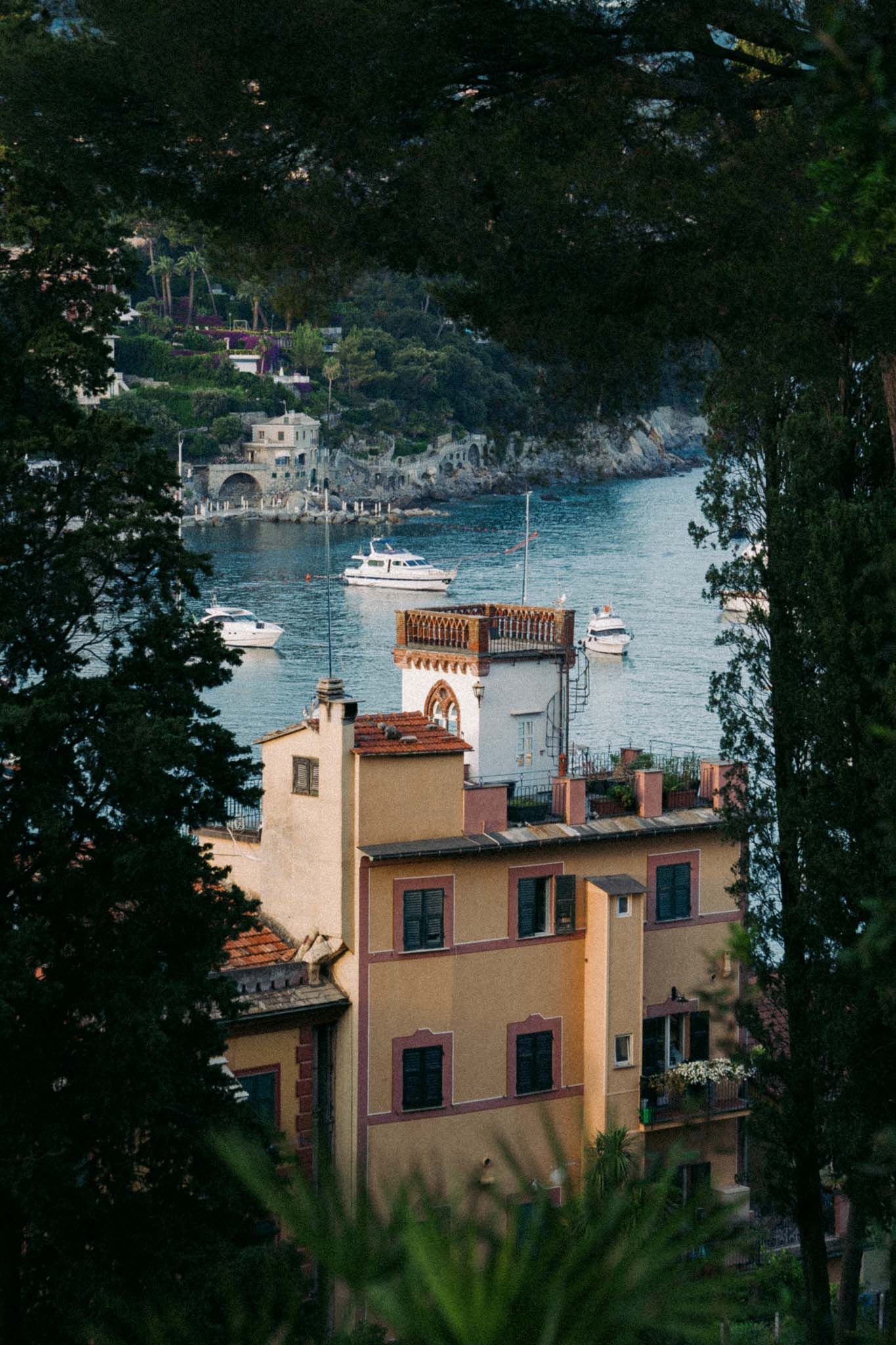 Mediterranean villa with terracotta roof overlooks a tranquil bay surrounded by lush trees and boats in the water.