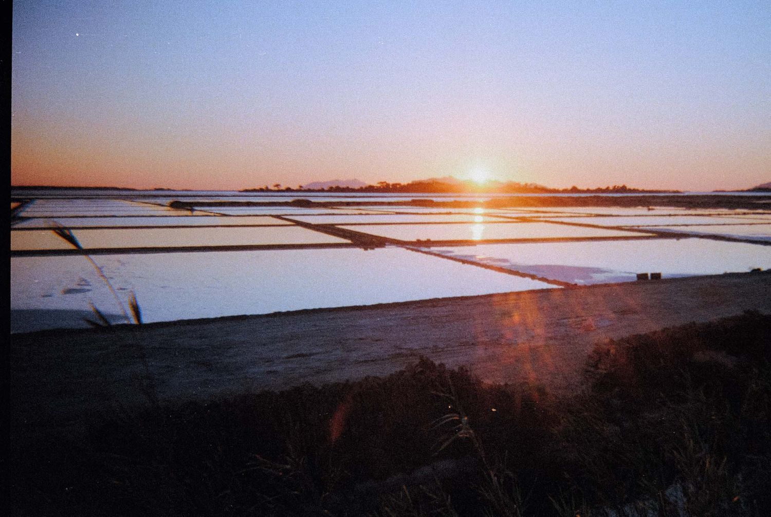 Panoramic sunset views over a salt flat landscape with warm orange light reflecting off the water's surface.