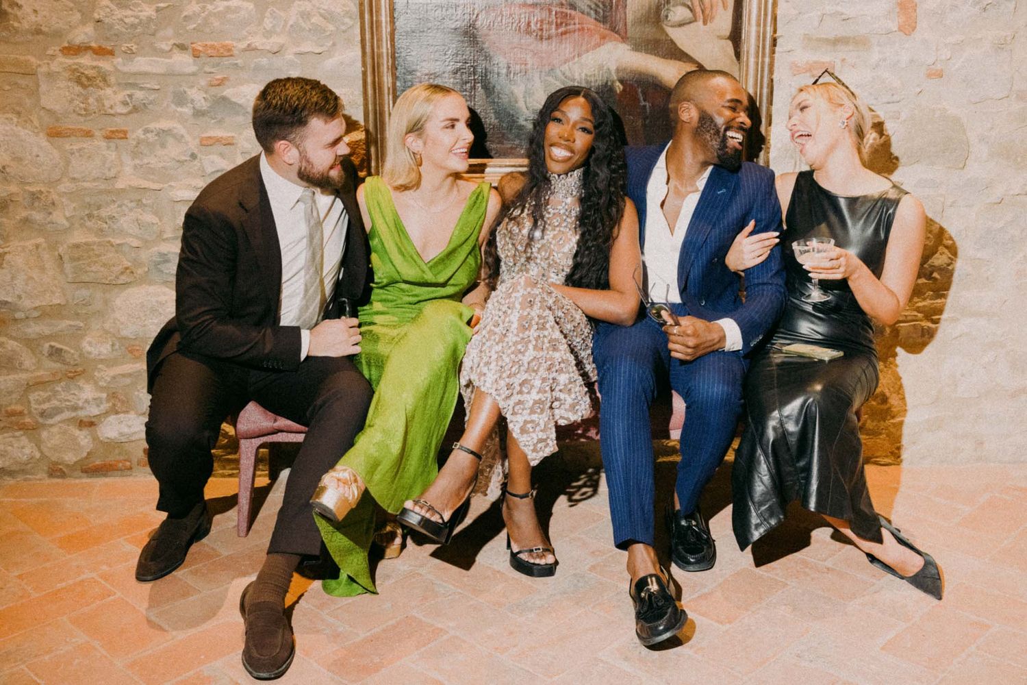 A group of people sitting together on a couch at a social gathering with exposed brick walls in the background.