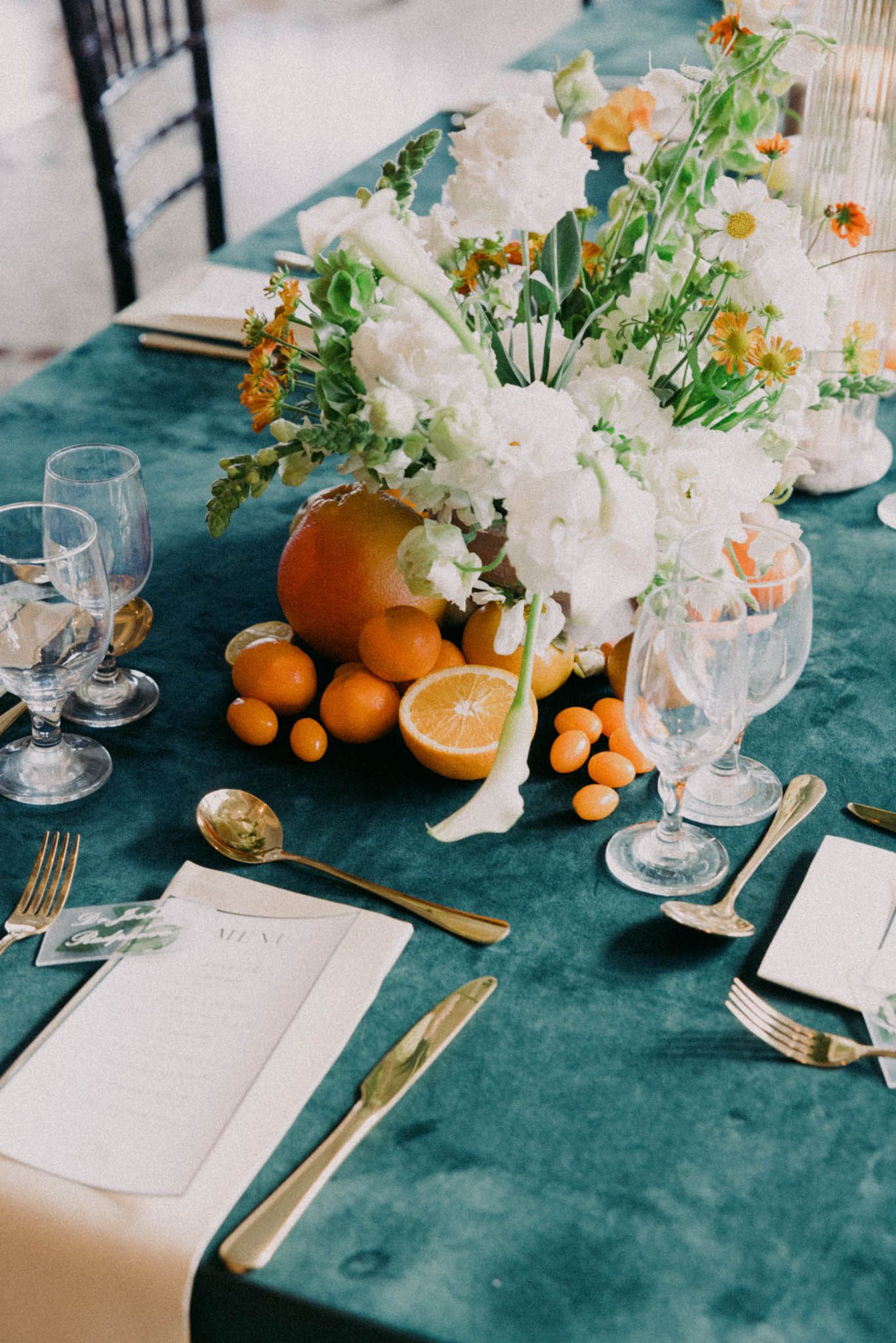 Elegant table setting with teal velvet tablecloth, fresh oranges, white floral arrangements and crystal glassware.