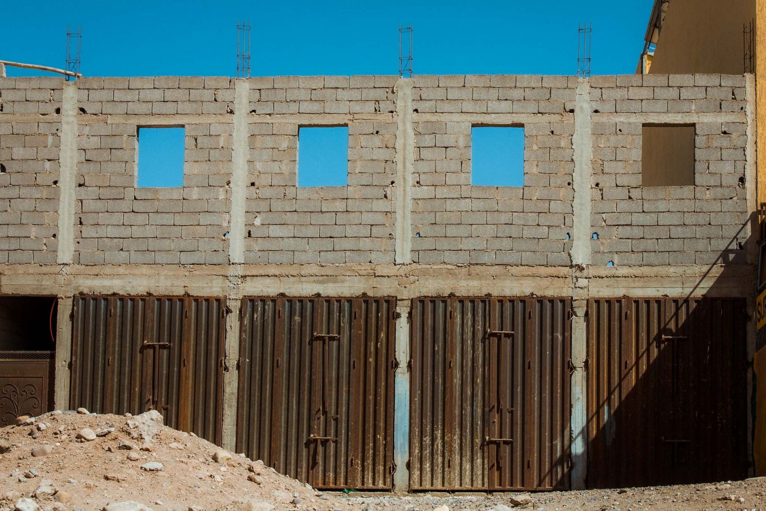 Unfinished concrete block building with wooden fencing and construction debris visible against a bright sky.