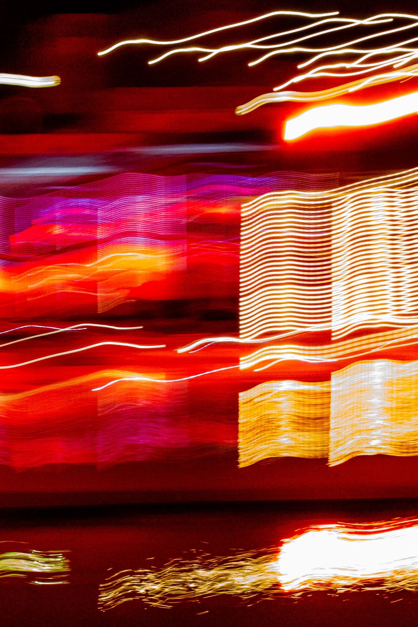 Long exposure light trails create abstract red and orange streaks against a dark background in a dynamic pattern.