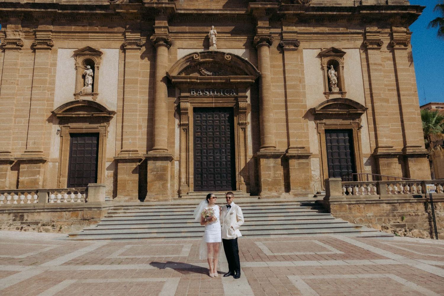 Historic stone cathedral facade with ornate architectural details and steps under bright blue sky in Sicily, Italy.