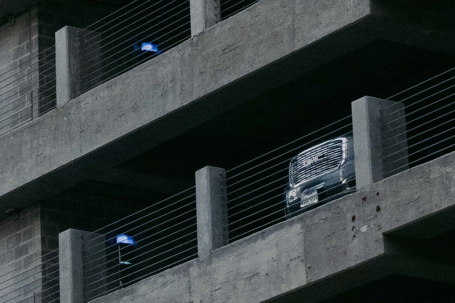 A car parked in a concrete parking garage with blue lights visible in the dark structure.
