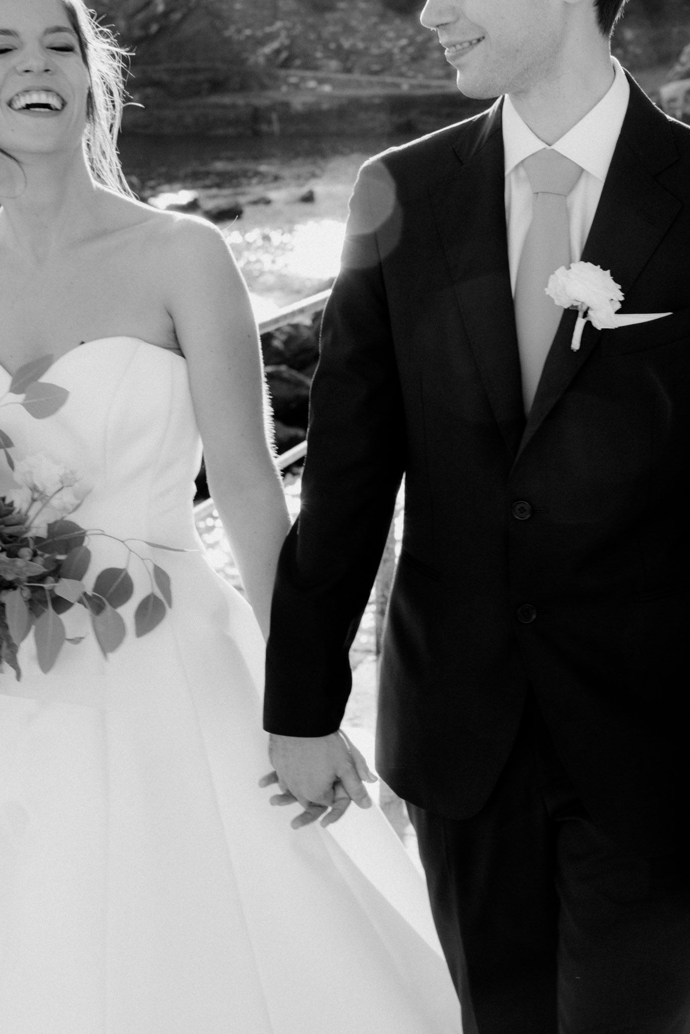 A black and white wedding photo showing a couple and wedding party laughing together outdoors.