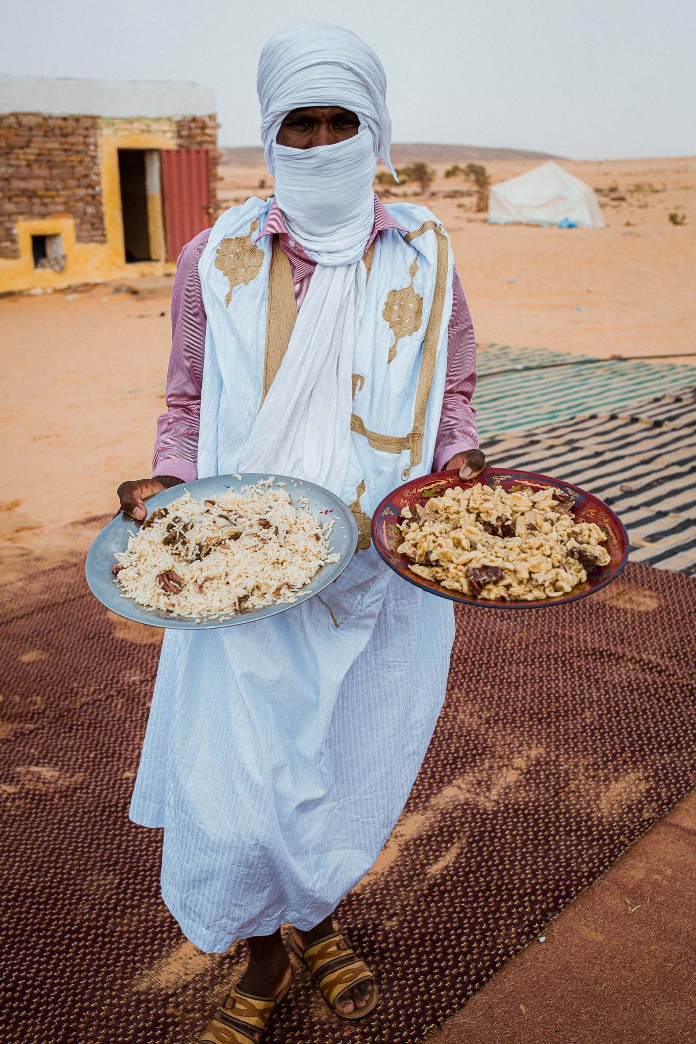 Traditional Moroccan couscous meal served on large plates in the Sahara Desert against a rustic backdrop.