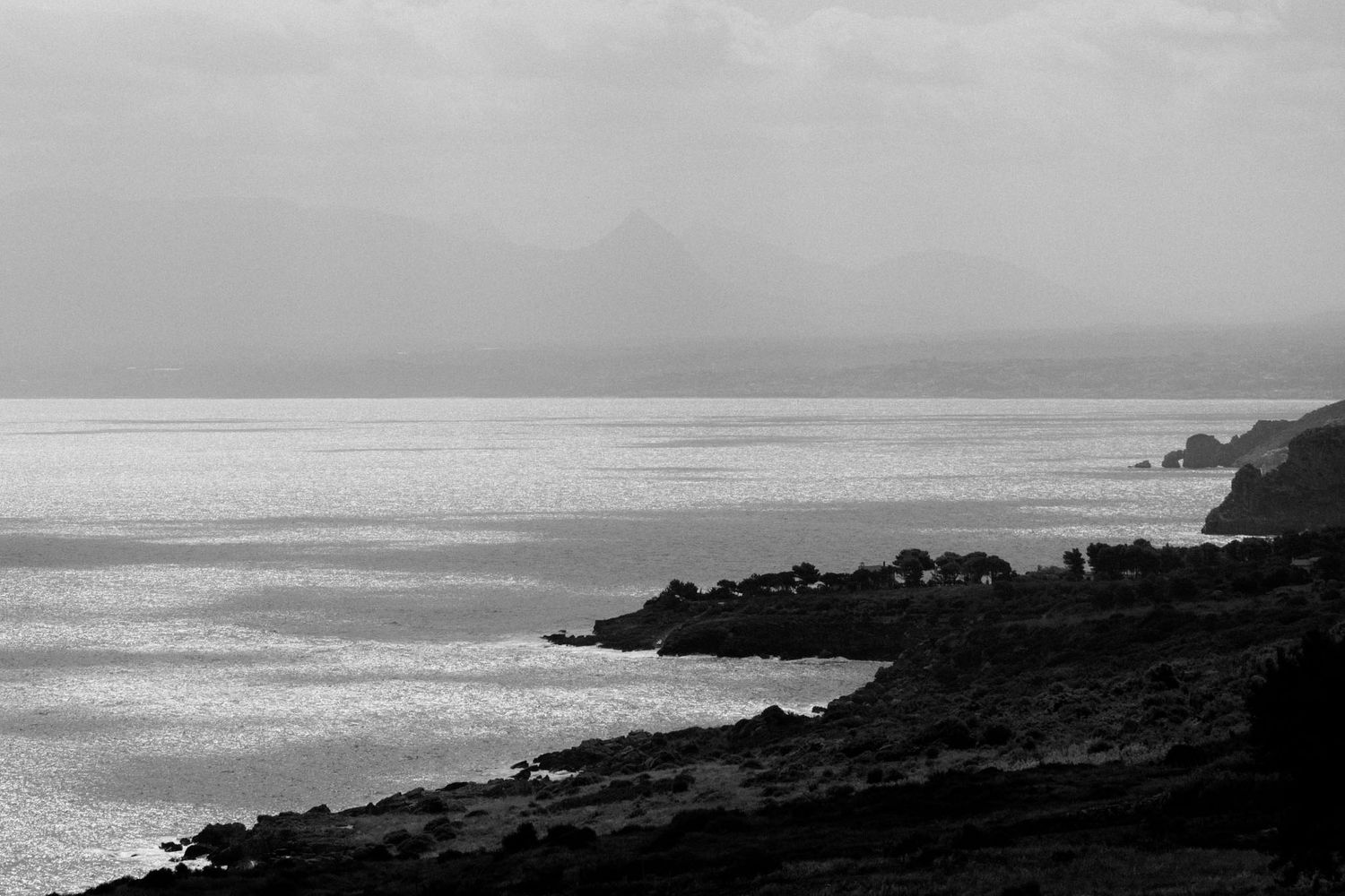 Dramatic black and white coastal landscape with rocky cliffs and crashing waves against a moody sky.