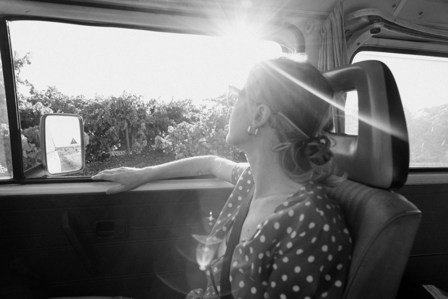 Black and white photo of someone in a polka dot dress sitting in a car with sunlight streaming through the window.