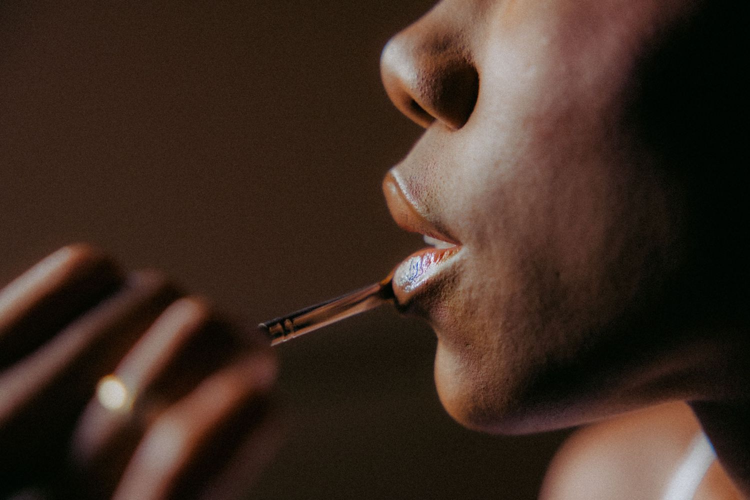 Close-up shot of someone applying pink lipstick with a makeup brush in warm lighting.