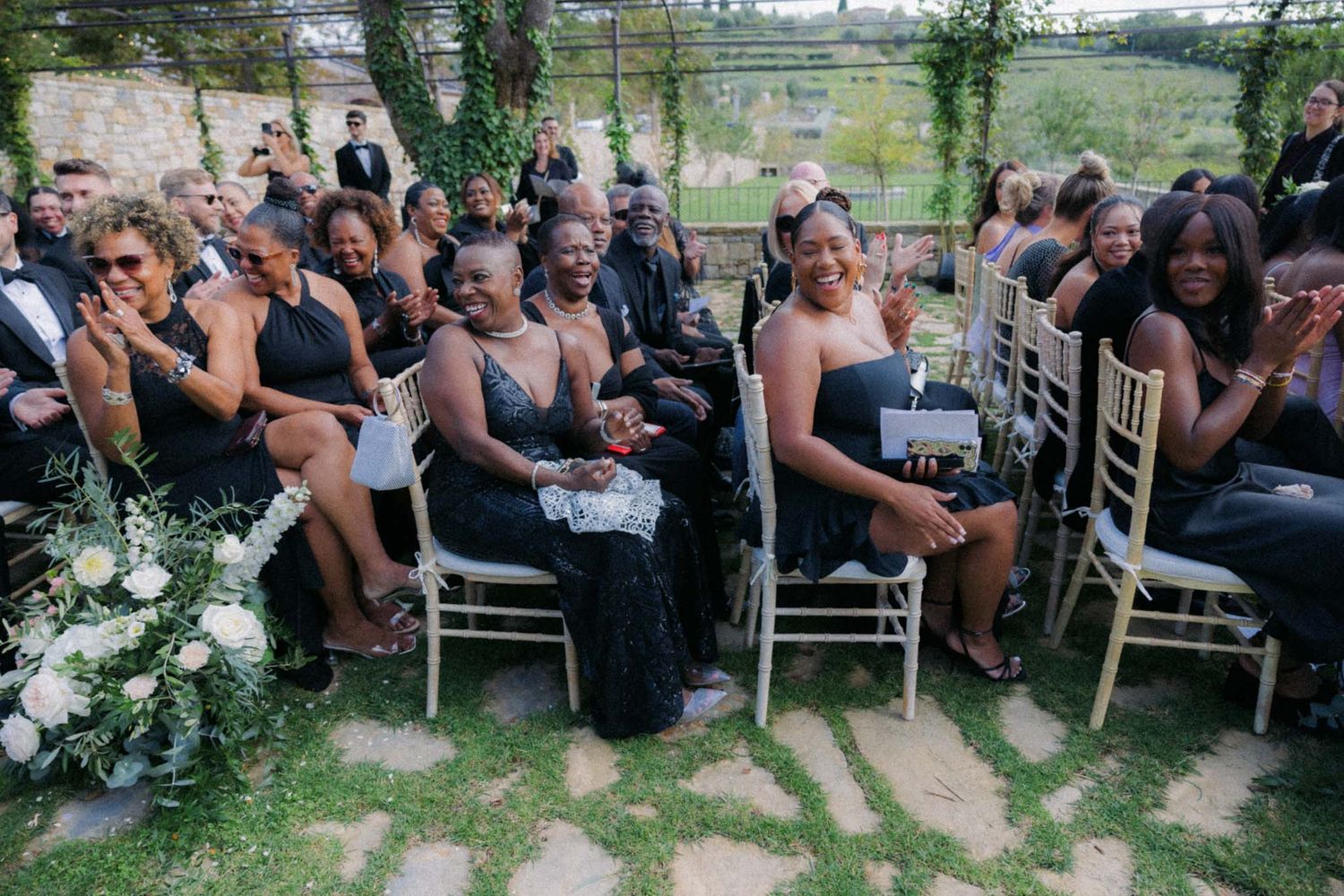 Wedding guests seated in white chairs on a grassy lawn during an outdoor summer ceremony.