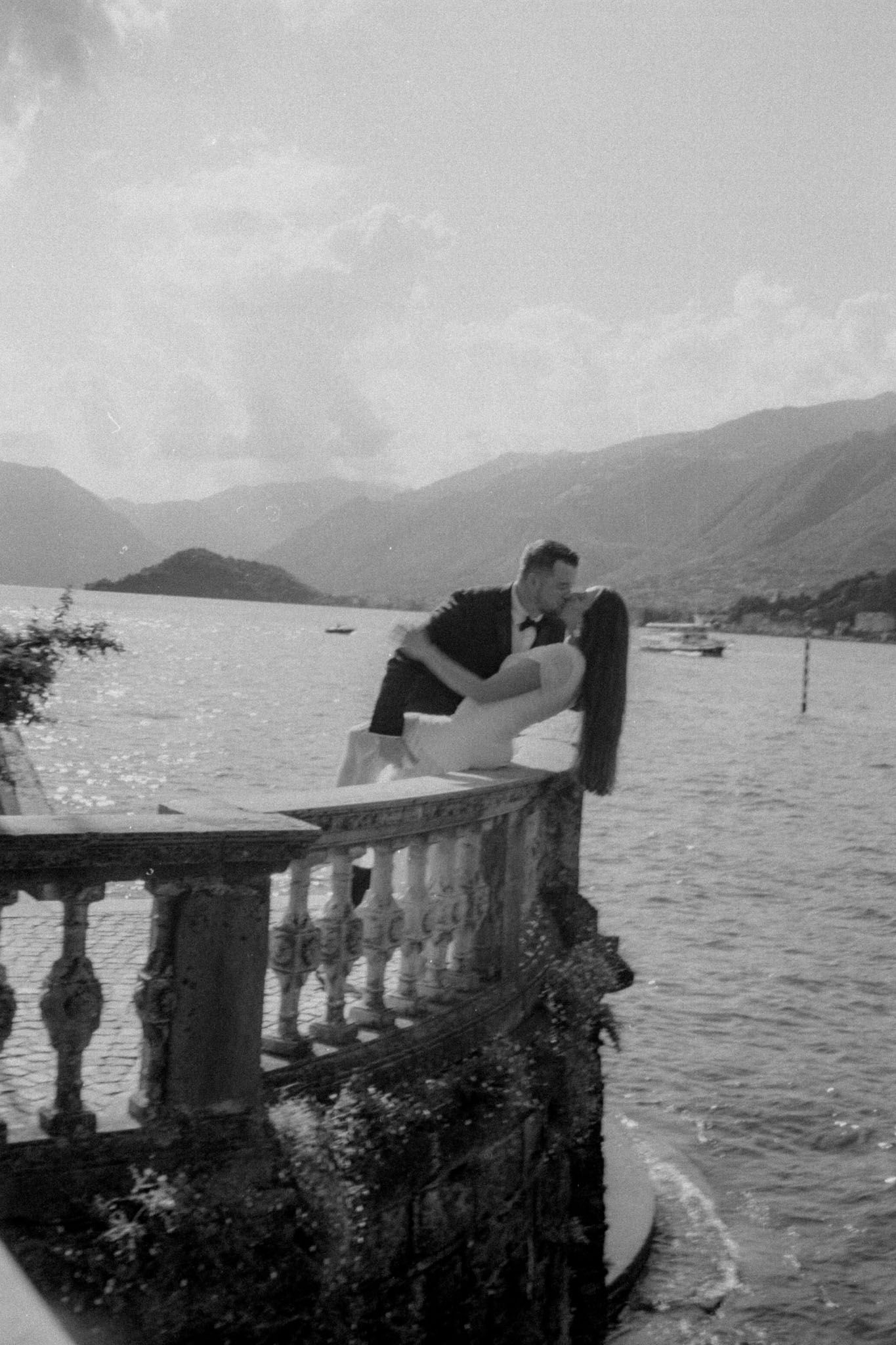 Black and white photo of a seaside balustrade with mountains and water in the background.
