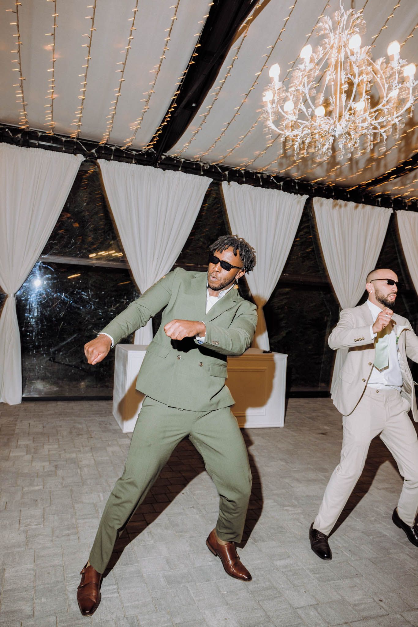 A sequence of dance moves showing two men in coordinated outfits performing energetic moves on a dance floor under chandeliers.