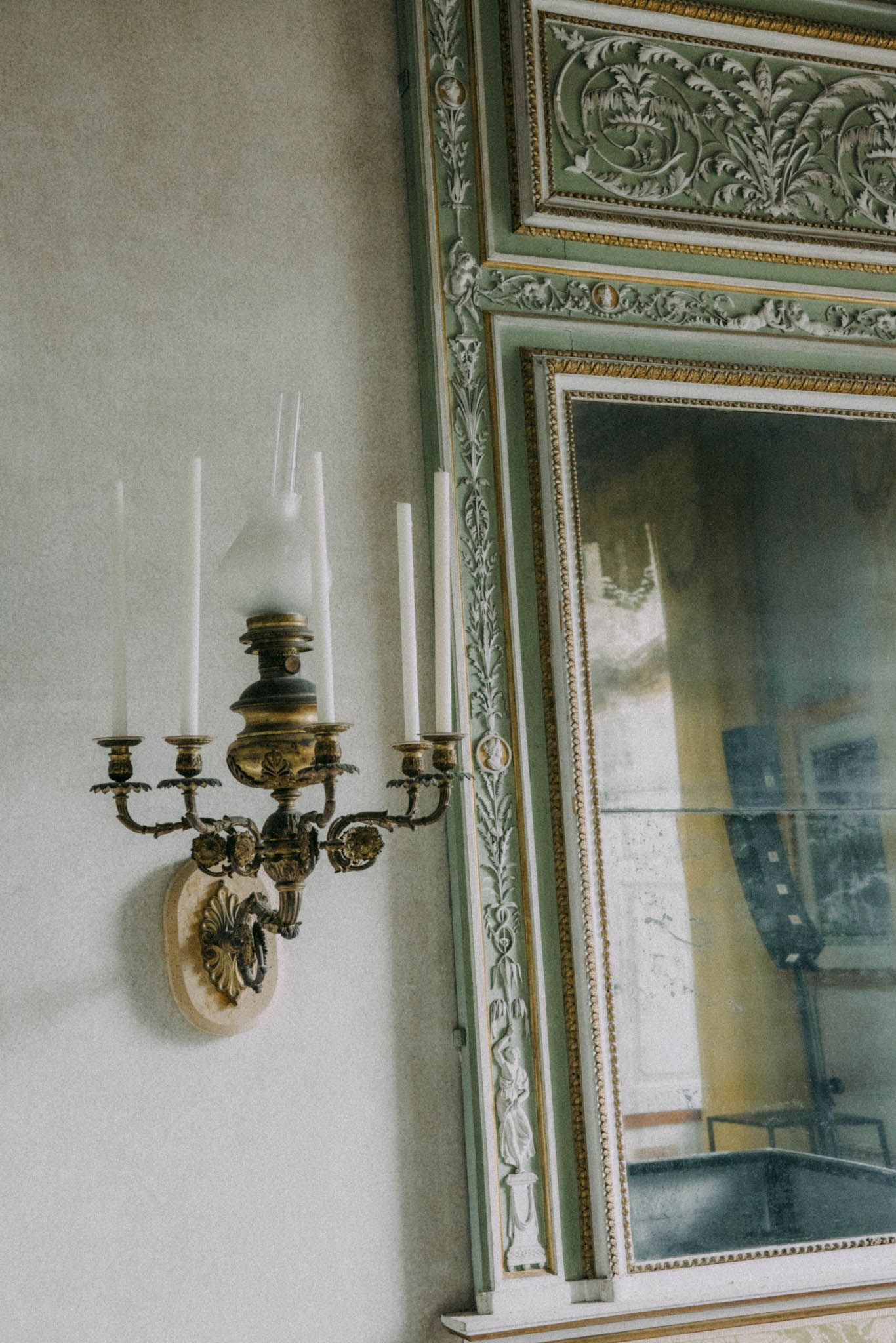 An ornate brass wall sconce with multiple candle holders mounted next to a decorative framed mirror with intricate molding.