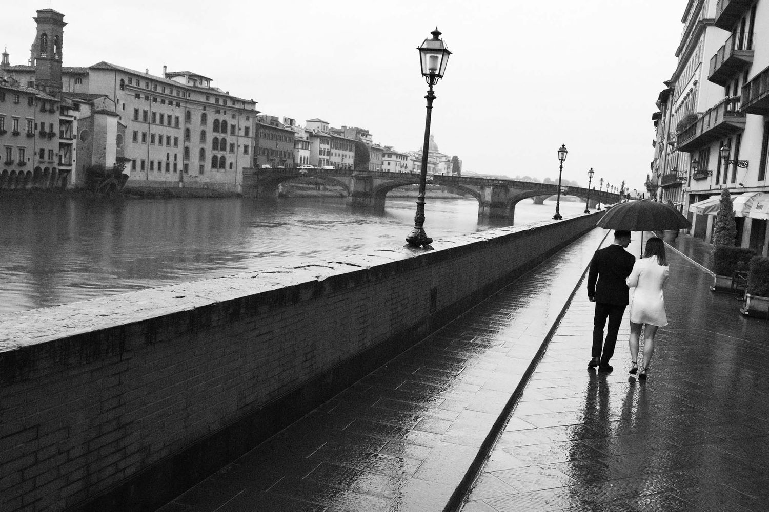 A series of black and white photographs showing people walking along a riverside promenade in Florence, Italy during rainy weather.