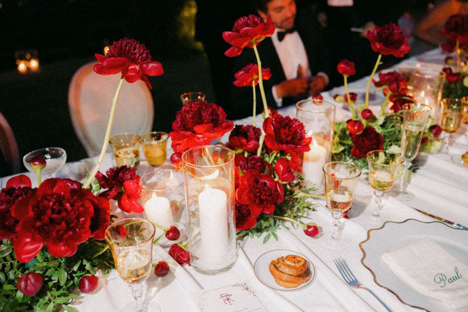 Elegant wedding reception tables decorated with vibrant red roses and glowing candles create a romantic atmosphere.