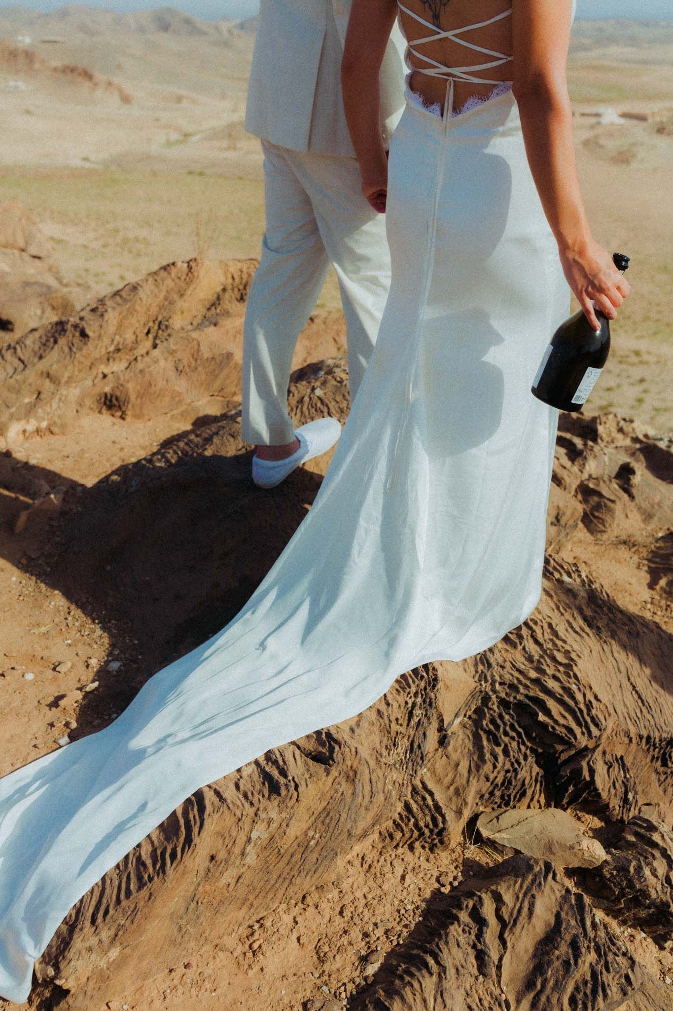 A white wedding dress flowing elegantly against a desert mountain landscape with rocky terrain.