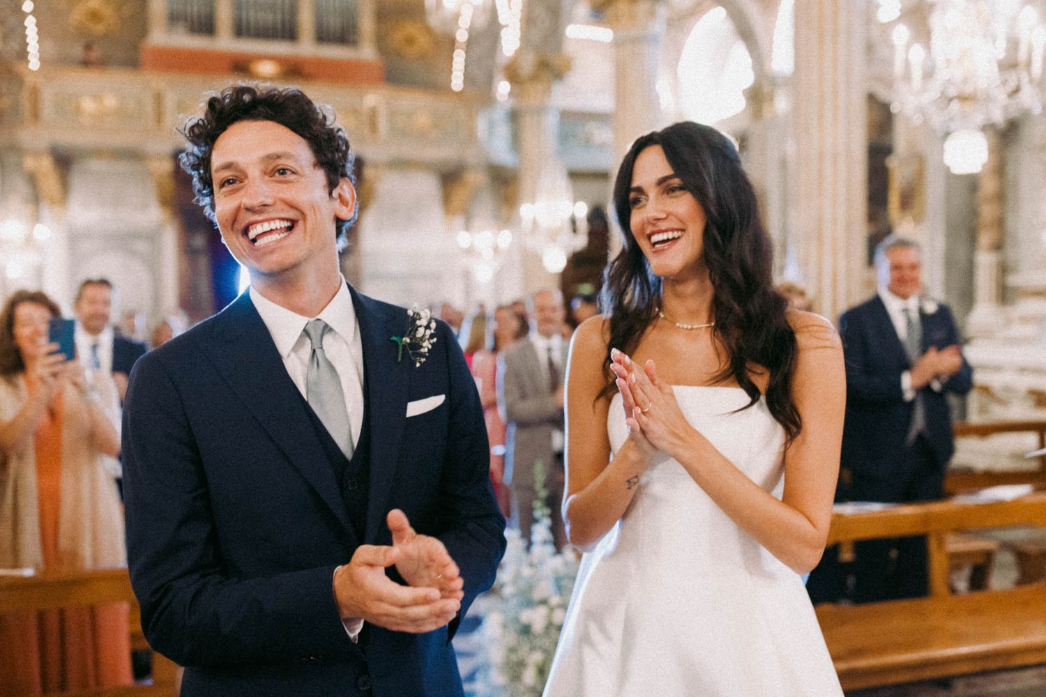 Joyful wedding celebration inside an ornate church with elegant chandeliers and classical architecture.