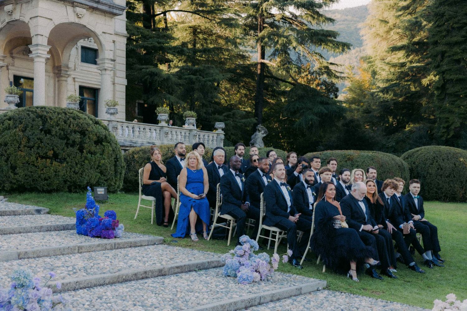 A series of wedding party group photos arranged on stone steps in an outdoor garden setting during daytime.