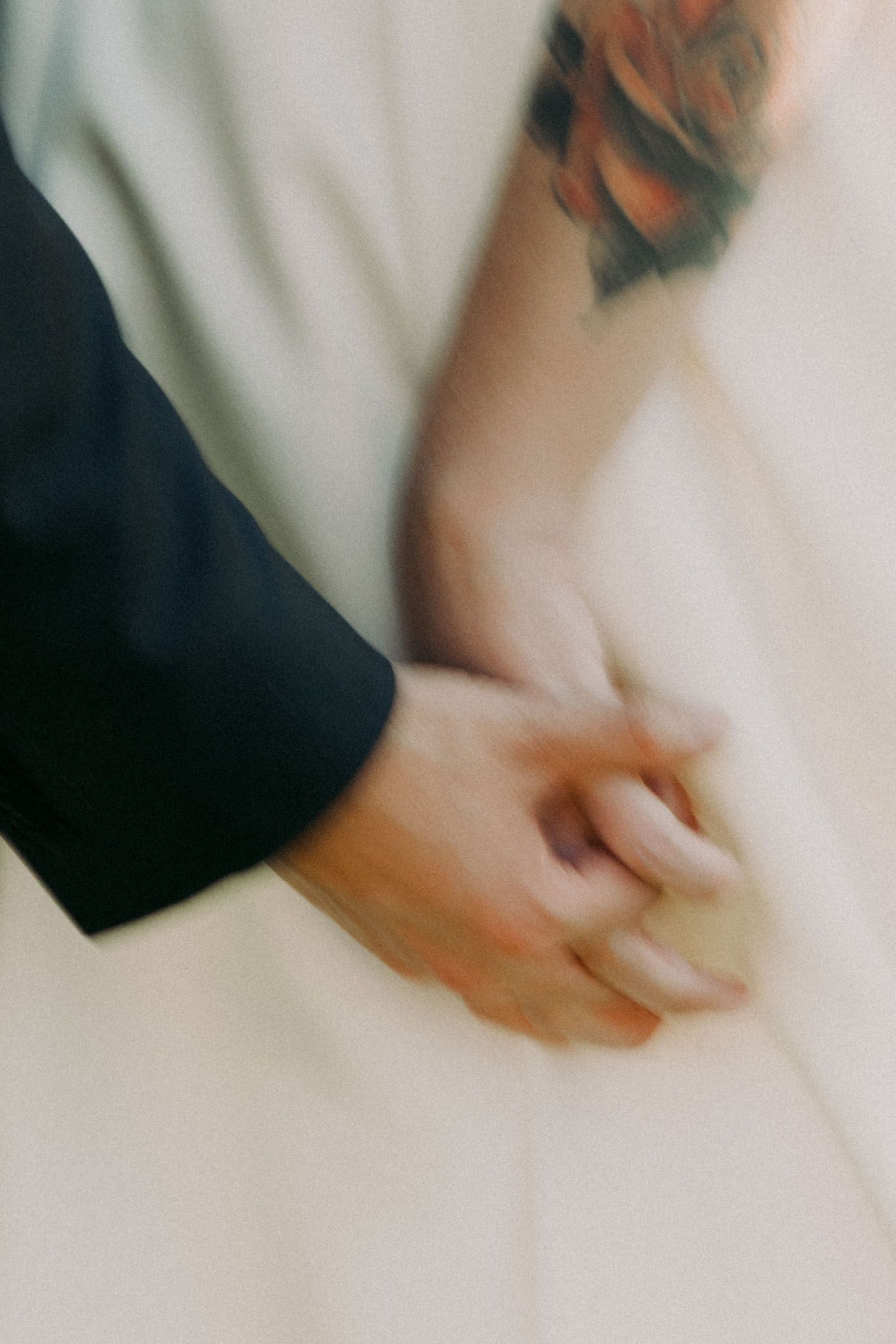 A close-up motion blur photo shows clasped hands with a visible tattoo against a light background.