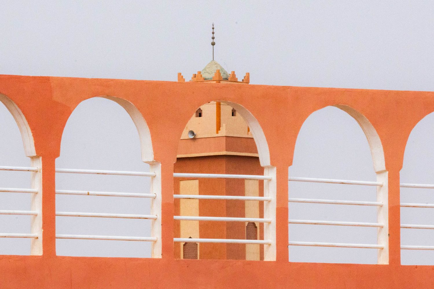 Orange and white architectural arches frame a domed tower against a pastel sky in a minimalist composition.