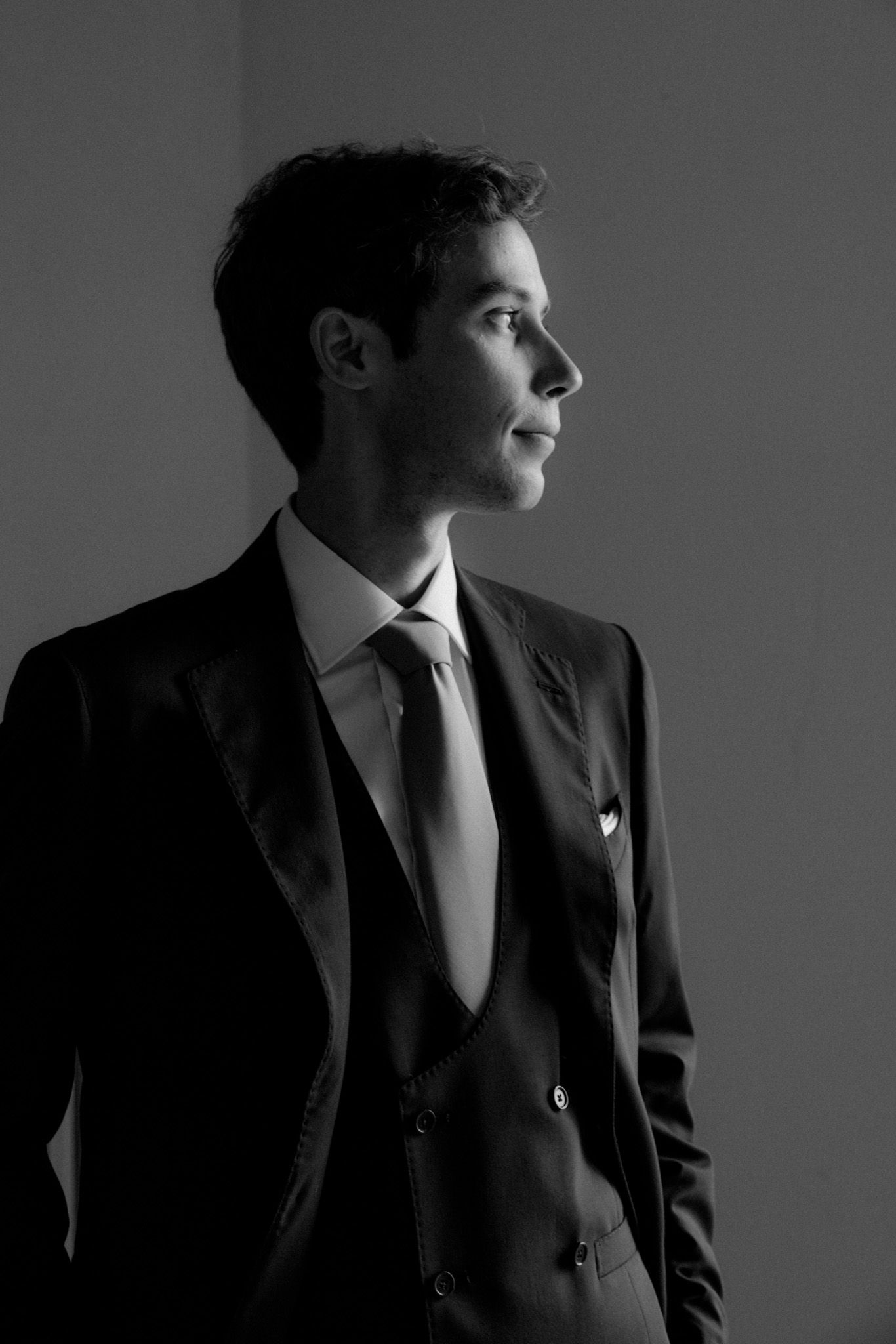 Dramatic black and white portrait series showing profile angles of person in dark suit against simple background.