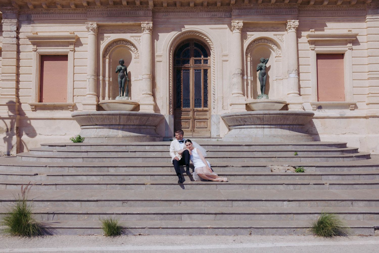 Stone steps lead up to an ornate classical building entrance with pale pink walls and architectural details.