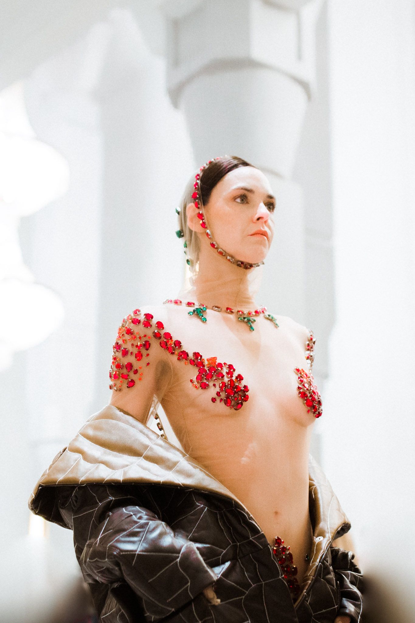 Artistic fashion portrait in white studio with red floral embellishments and dramatic lighting.