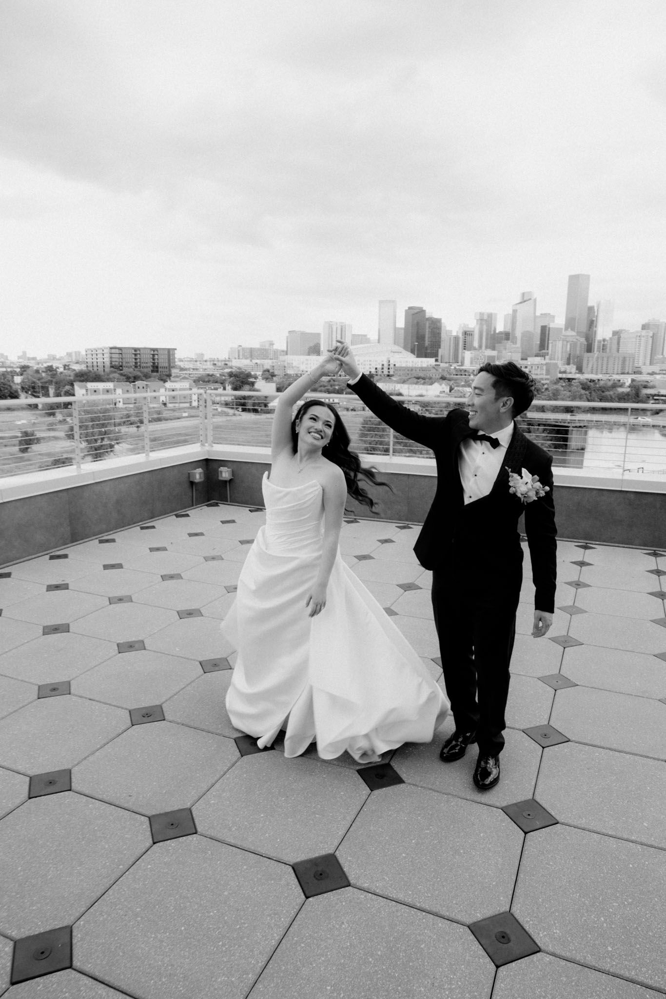 A couple dancing and twirling on a rooftop terrace with geometric patterned flooring and city skyline in background.