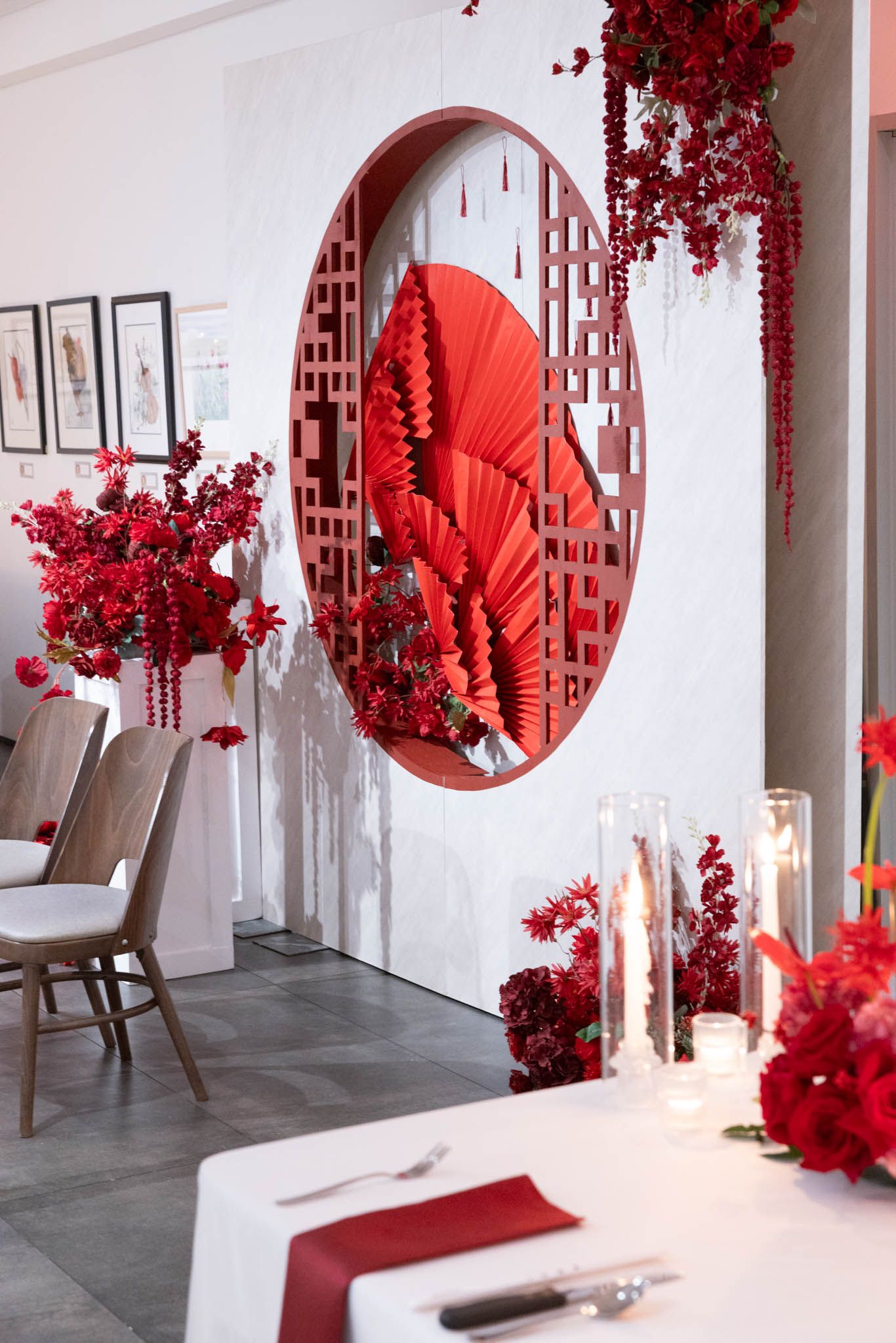 Modern restaurant interior featuring dramatic red floral arrangements and circular wall accents against white walls.