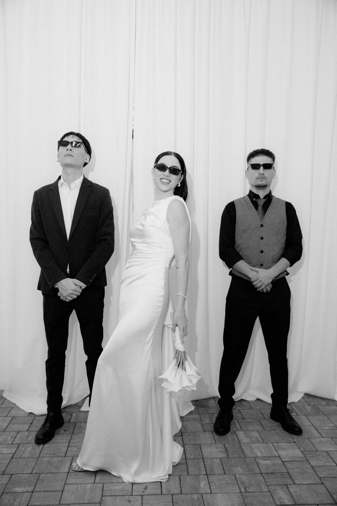 A series of black and white photos showing figures in contrasting dark suits and white outfits posing against a wall.