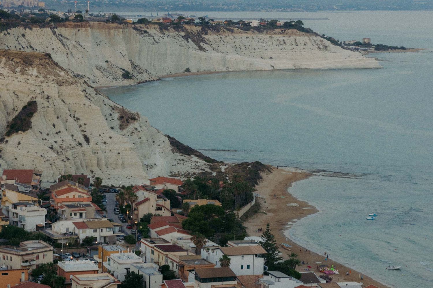 Aerial panoramic view of coastal Mediterranean town with sandy beaches and rocky cliffs along turquoise waters.