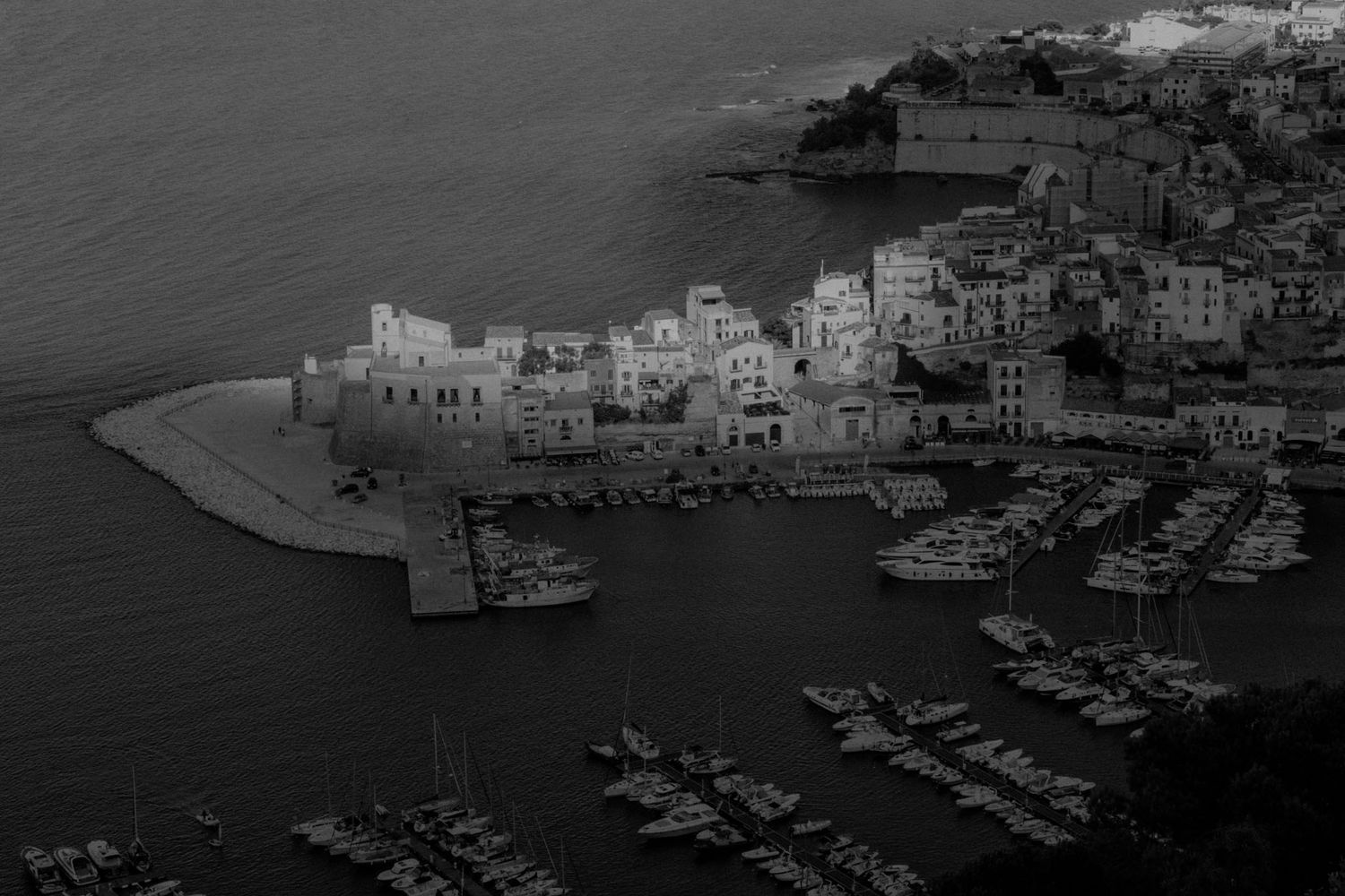 Panoramic black and white aerial view of a Mediterranean coastal town with white buildings and boats in the harbor.