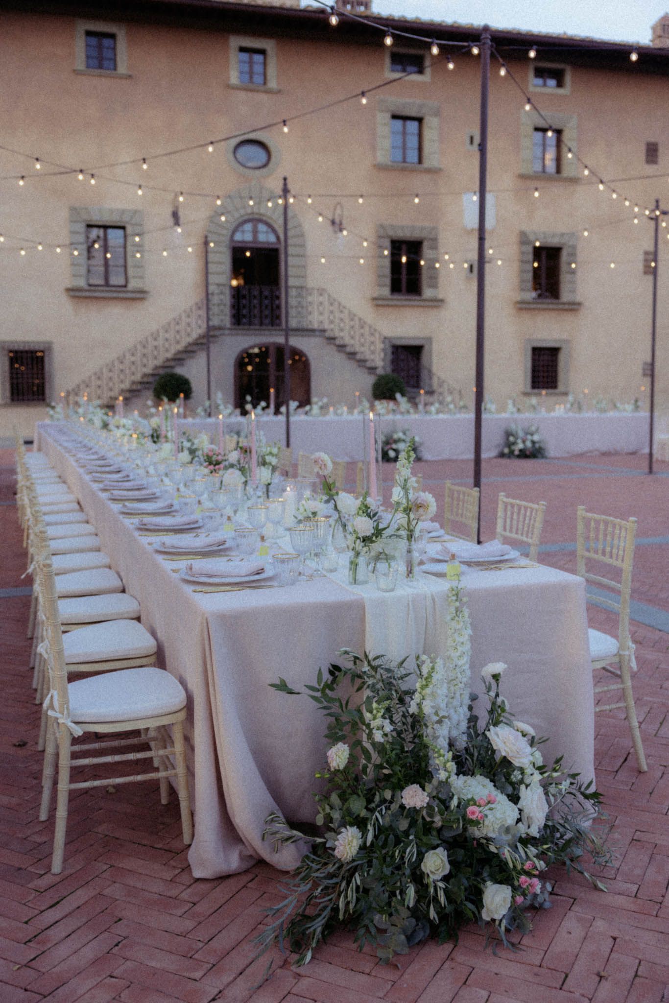 Elegant outdoor wedding reception table with white linens, string lights, and lush floral arrangements at a rustic Italian villa.