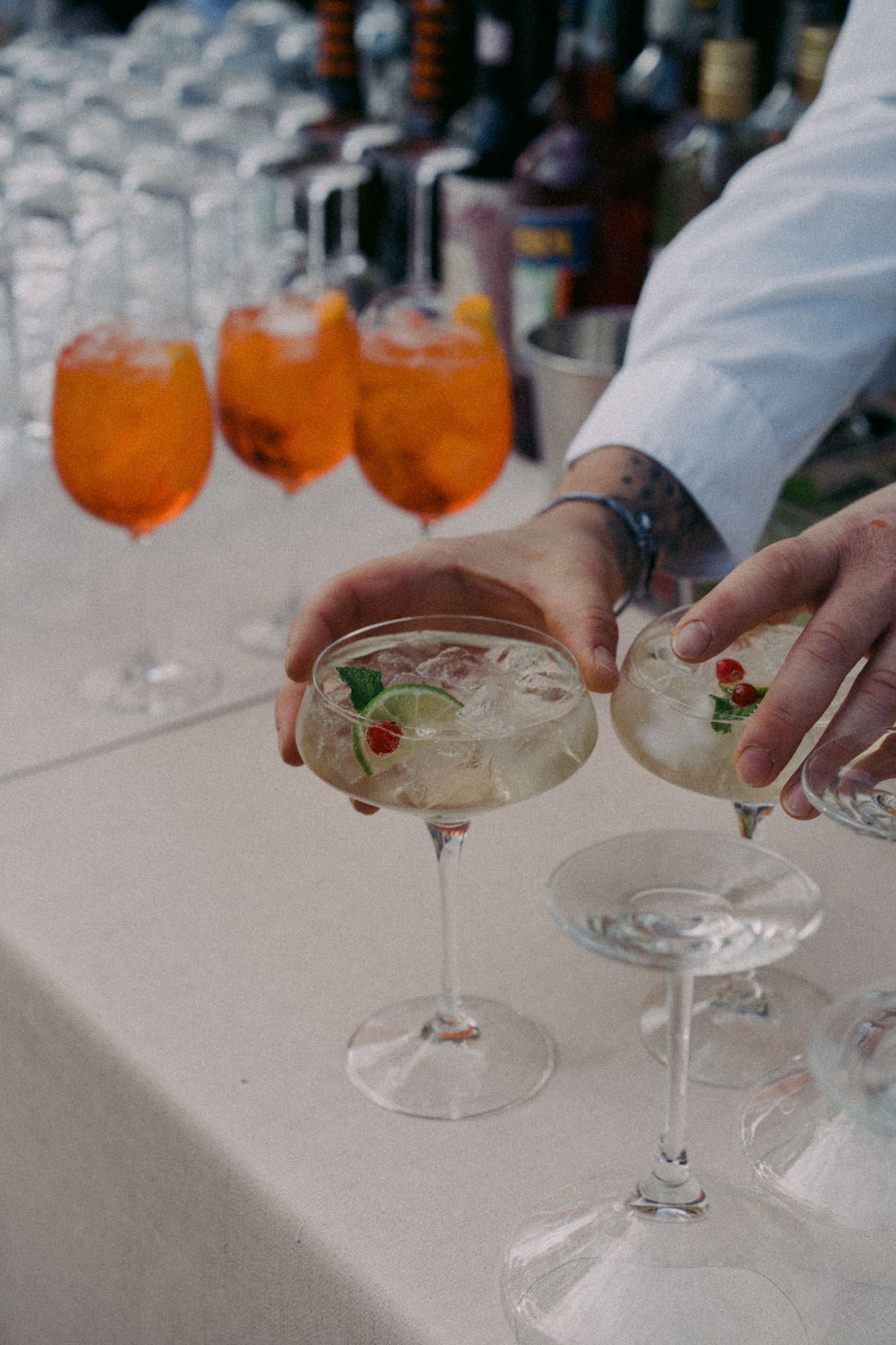 Hands garnishing cocktail glasses with fresh herbs at an upscale bar with orange drinks in the background.