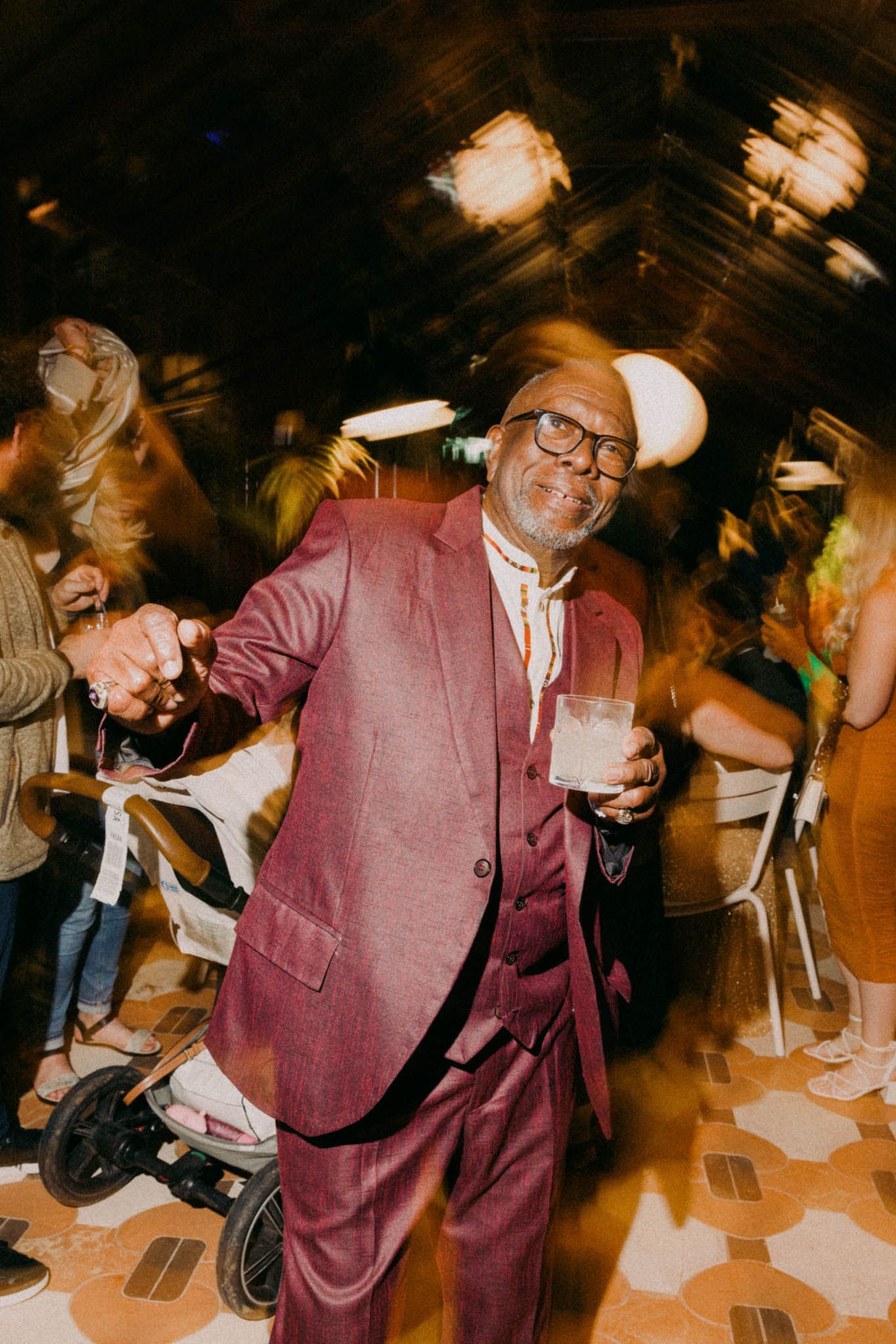 Person in a burgundy suit dancing energetically at a party with motion blur effects creating a dynamic atmosphere.