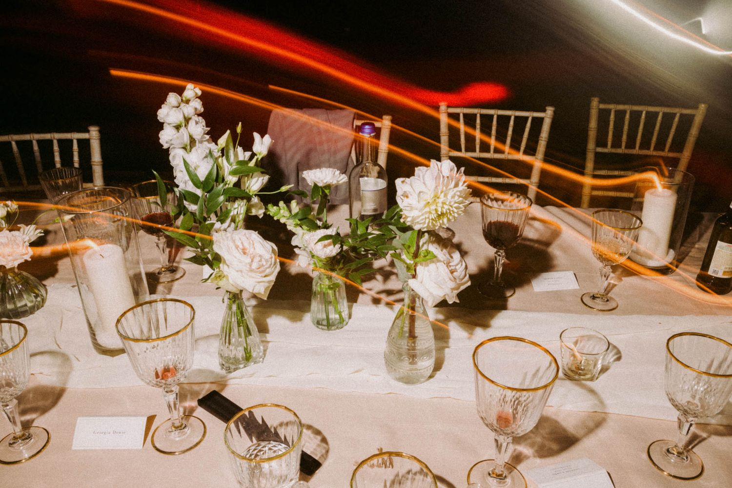 Elegant wedding reception tables decorated with white floral centerpieces and gold-rimmed glassware in a dimly lit venue.