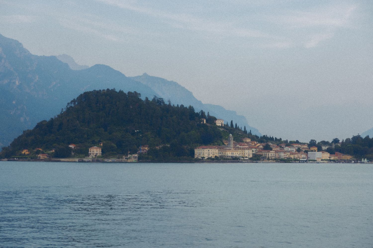 Scenic lakeside view of Italian coastal towns surrounded by mountains along Lake Como's tranquil waters.