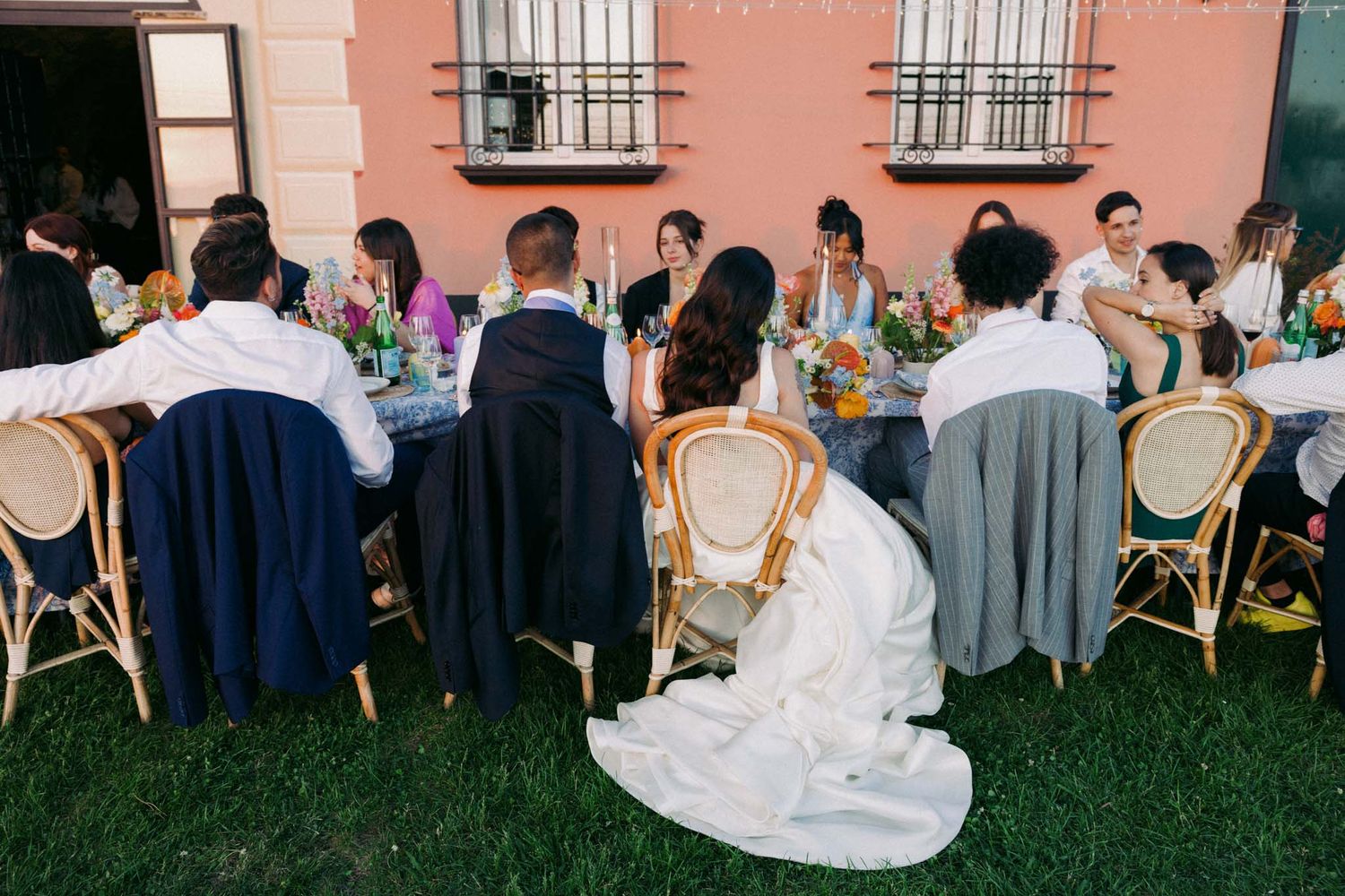 Wedding guests enjoy an outdoor reception on a lawn with tables and chairs arranged under string lights at dusk.