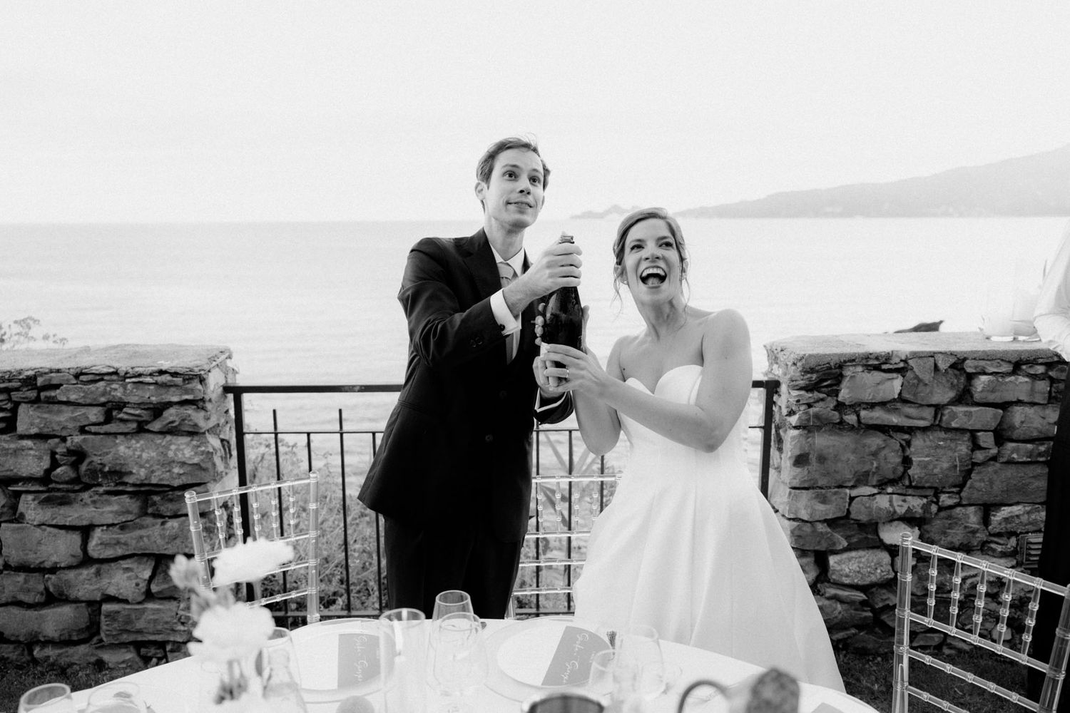 Black and white wedding photos show couple laughing and celebrating together on a stone terrace.