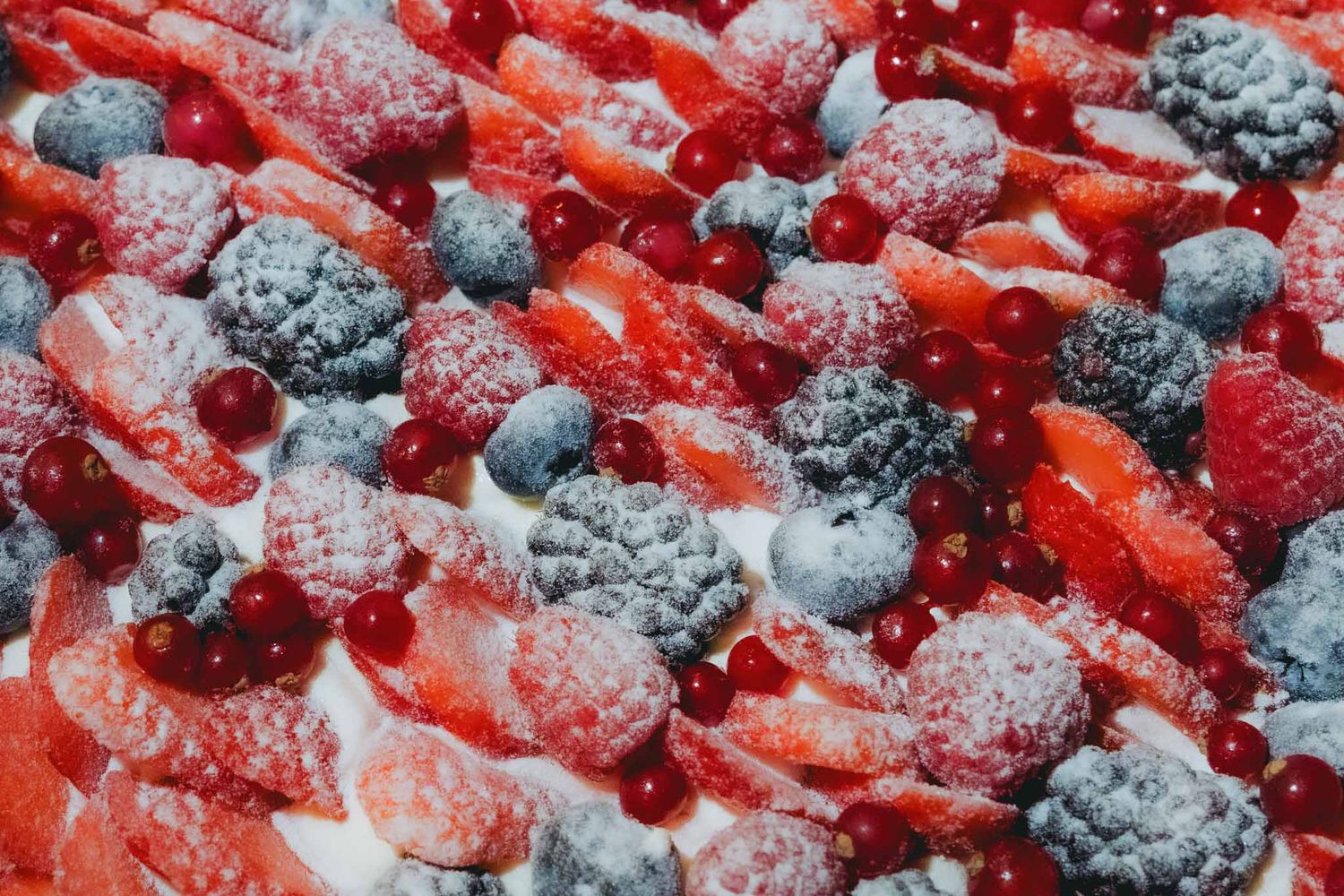 Fresh strawberries and blueberries dusted with powdered sugar create a vibrant red and blue dessert topping.