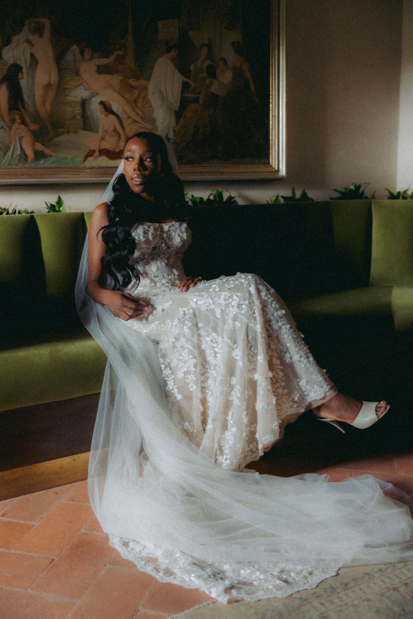 A bride in an elegant lace wedding gown poses gracefully on a terracotta floor with a flowing veil.
