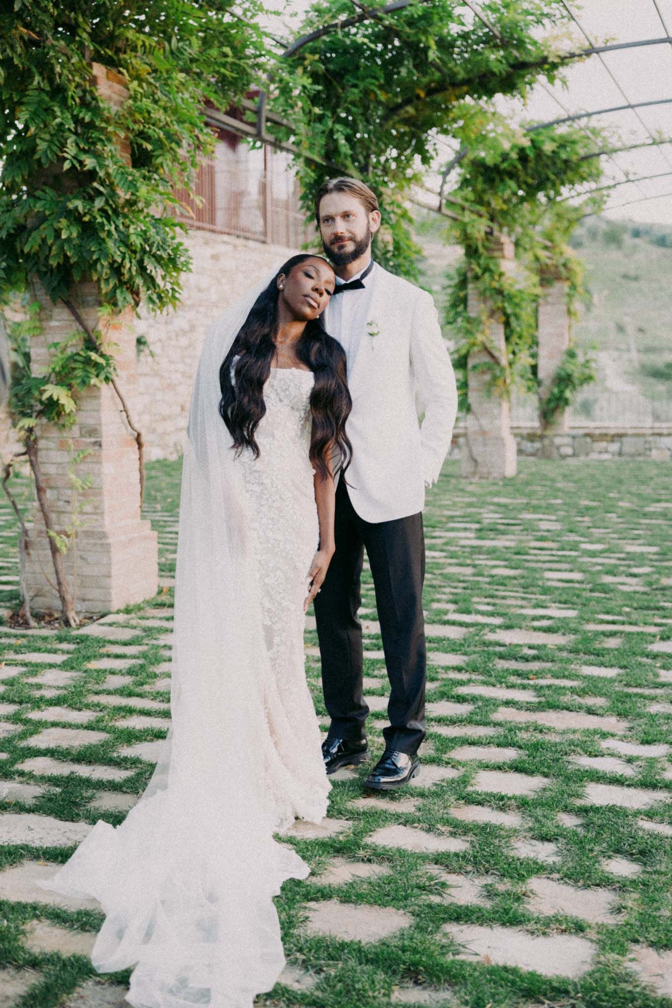 A couple shares a romantic moment in a garden with stone pavers and lush greenery overhead.