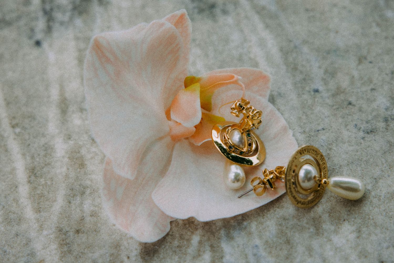 Delicate pink orchids and vintage-style jewelry arranged artistically on a textured gray stone surface.