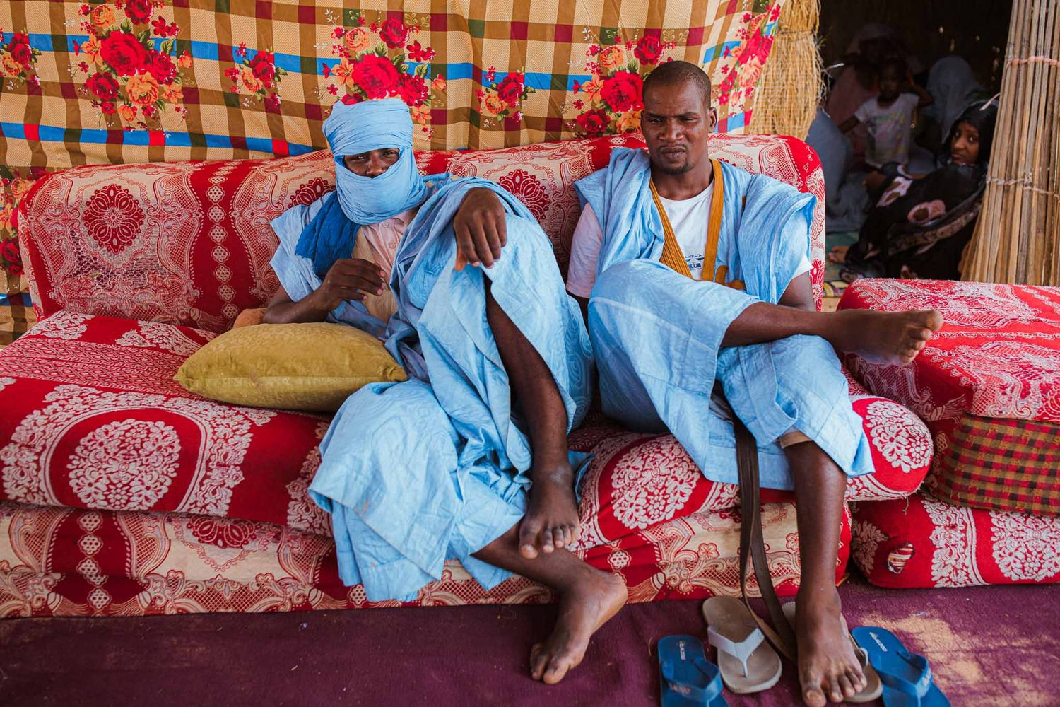 Group gathered on colorful patterned textiles in traditional setting.