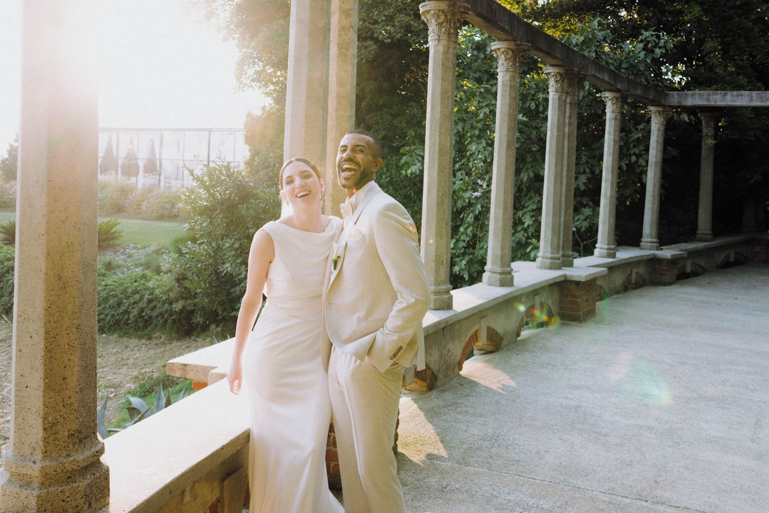 People in white clothing gather on a columned porch of a historic building on a sunny day.