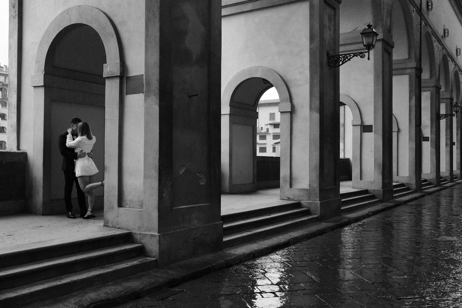 Black and white architectural photograph of arched colonnade hallway with dramatic shadows and perspective.