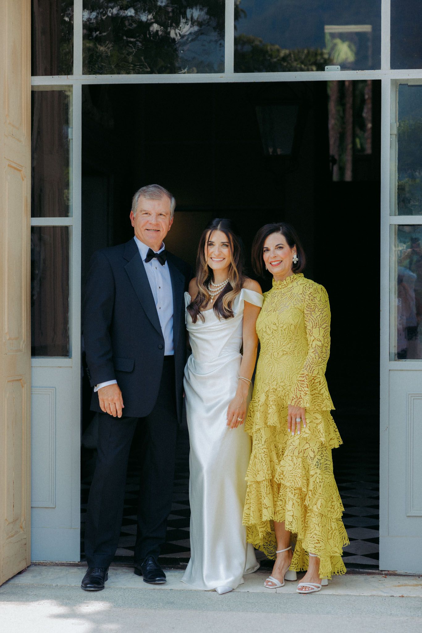 A group stands together on a porch wearing formal attire including a white dress and yellow ruffled dress.